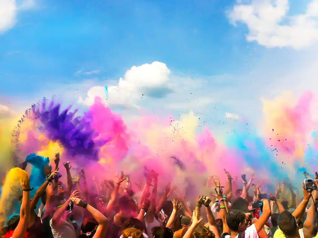 Crowds of people at a festival throwing coloured powder in the air