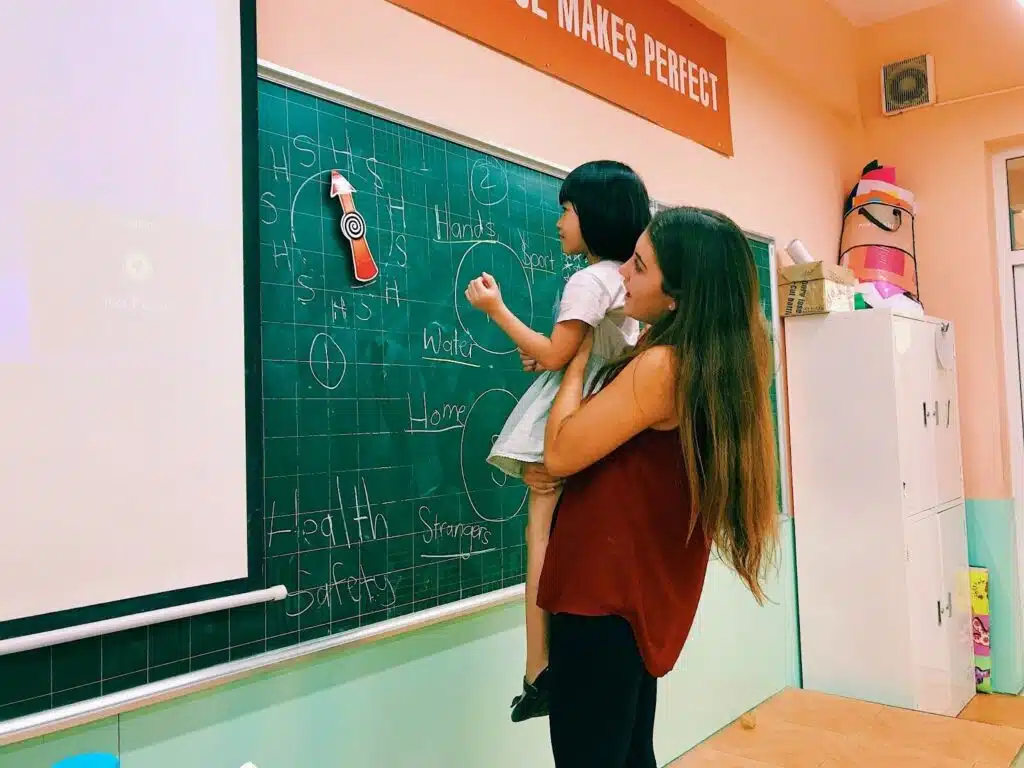 Teacher Taylor holding a young student up to write on a blackboard in Vietnam