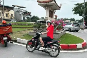 English teacher commuting through busy Hanoi city streets on motorbike